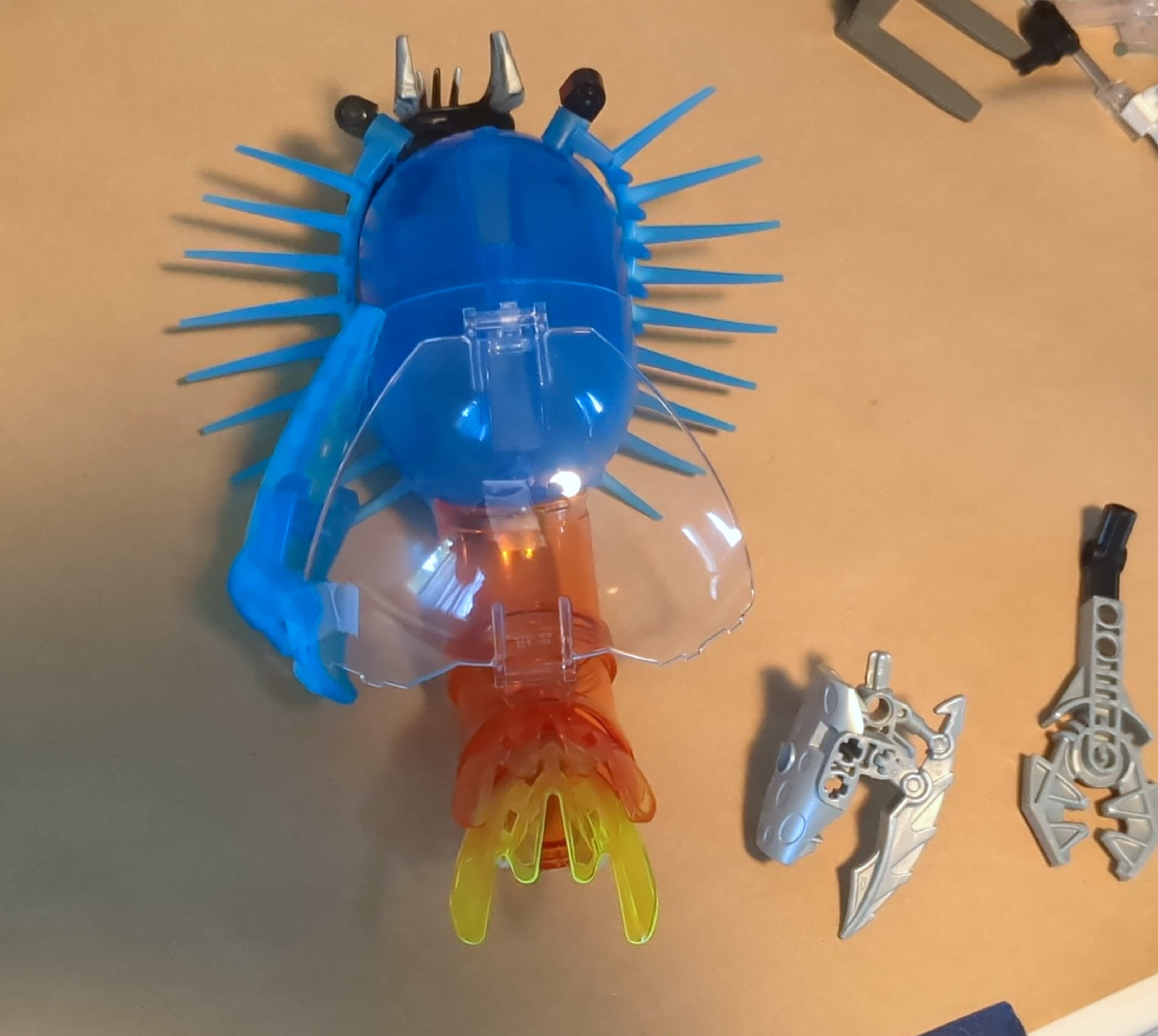 Transparent blue and orange elements arranged like a soft, spiny sea creature; silver claws lie next to it